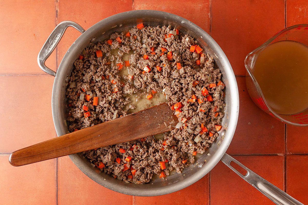 Overhead image of ground beef and vegetables simmering in a skillet with beef broth to create the rich shepherd’s pie sauce.