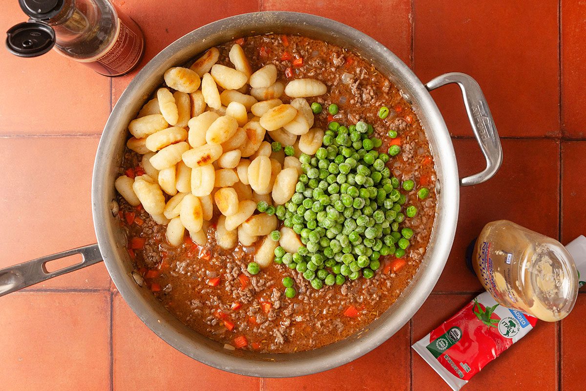 Overhead image of gnocchi, peas and beef mixture combined in a skillet with tomato paste and sauce for the finished gnocchi shepherd’s pie filling.