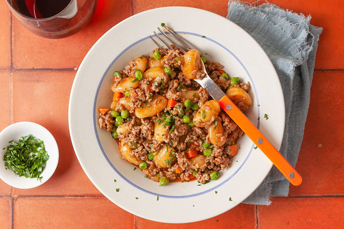 Overhead image of gnocchi shepherd’s pie served in a bowl with a fork, highlighting the hearty mixture of gnocchi, beef and vegetables.