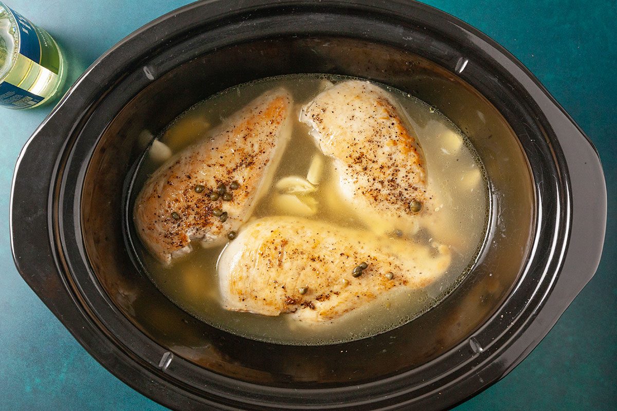 Overhead horizontal image of chicken breasts placed in a slow cooker with broth and lemon mixture.