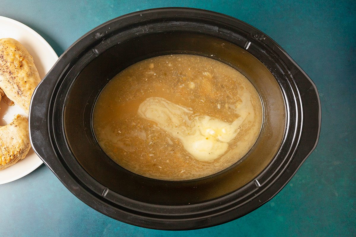 Overhead horizontal image of sauce in slow cooker with butter melting into lemon broth.