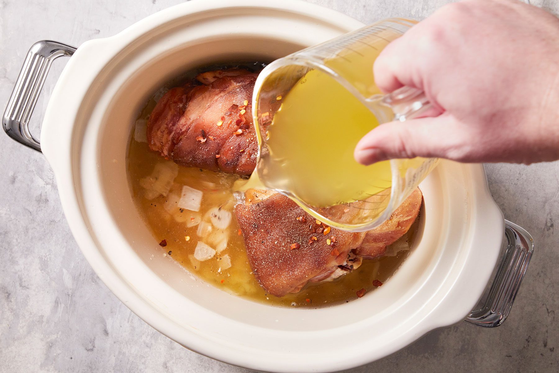 Adding chicken broth, water, the ham hock, salt, pepper and crushed red pepper flakes in a slow cooker.