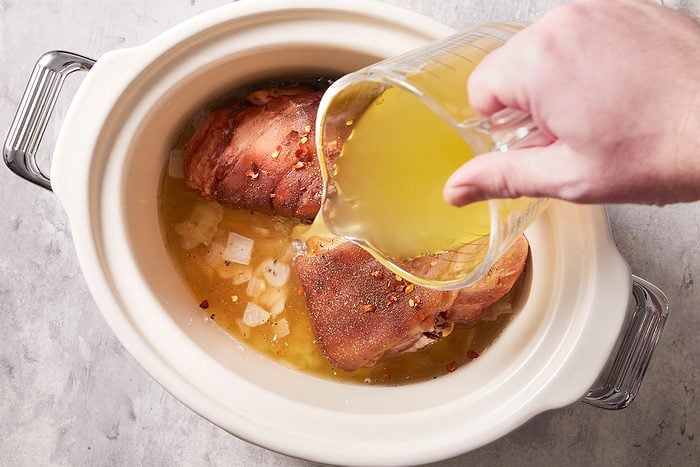 Adding chicken broth, water, the ham hock, salt, pepper and crushed red pepper flakes in a slow cooker.