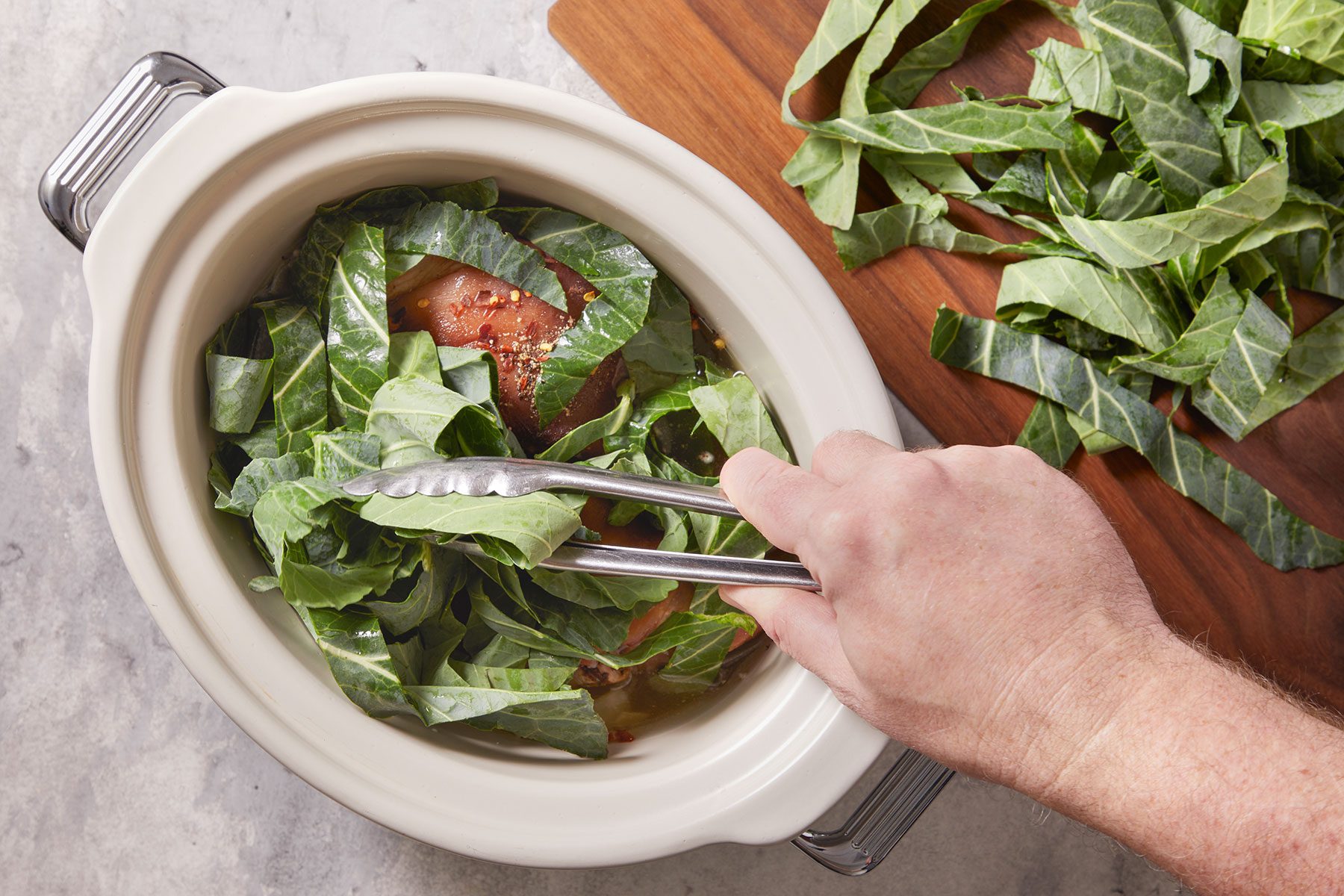 Adding collard strips to slow cooker full of ham and broth.