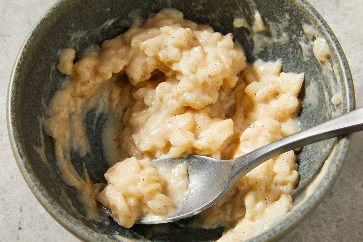Close-up shot of Slow-Cooker Rice Pudding being stirred in a pot with a spoon, highlighting the soft rice grains and creamy texture.