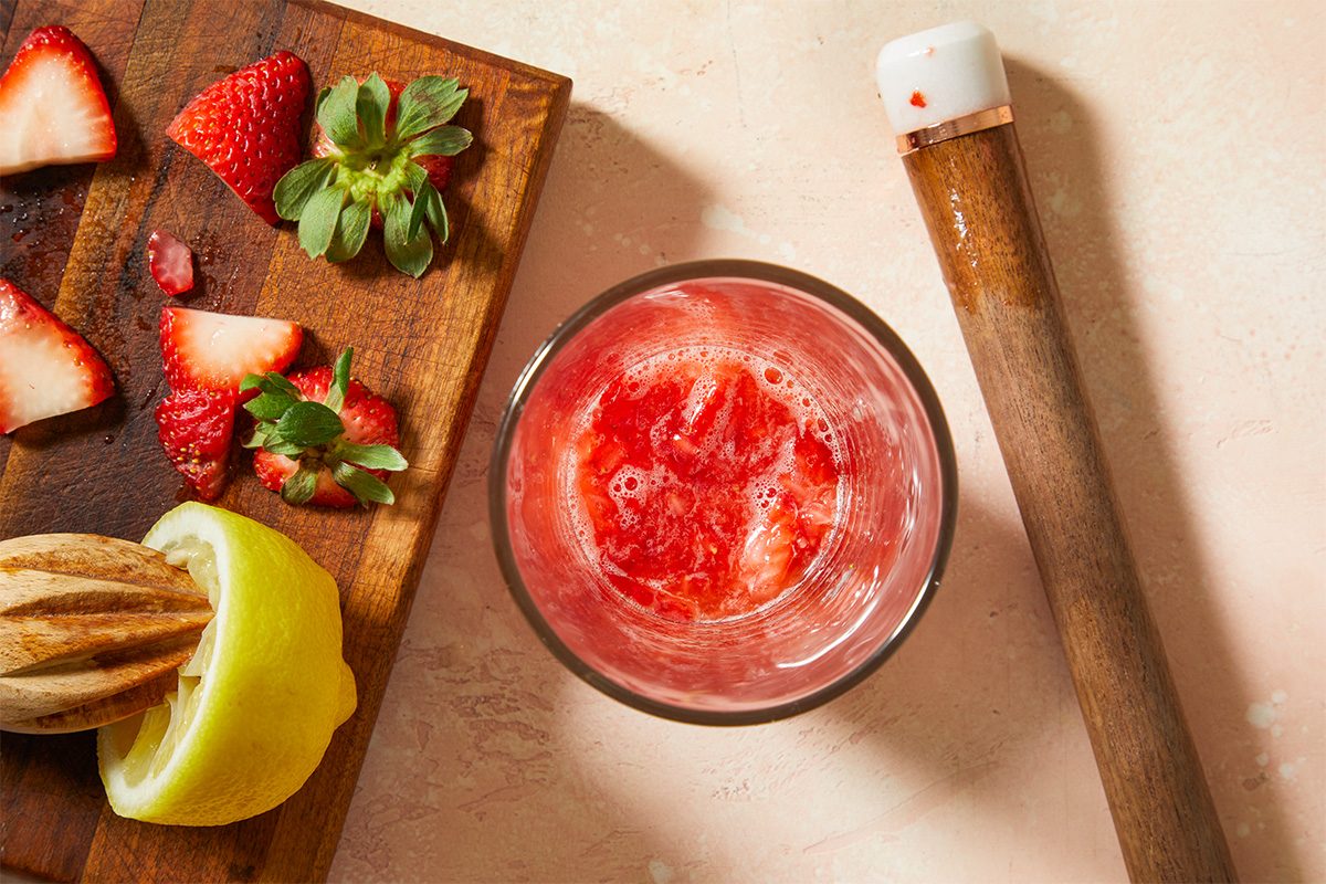 Overhead horizontal image of fresh strawberries, lemon, and a muddled strawberry mixture prepared for a strawberry lemon drop cocktail.
