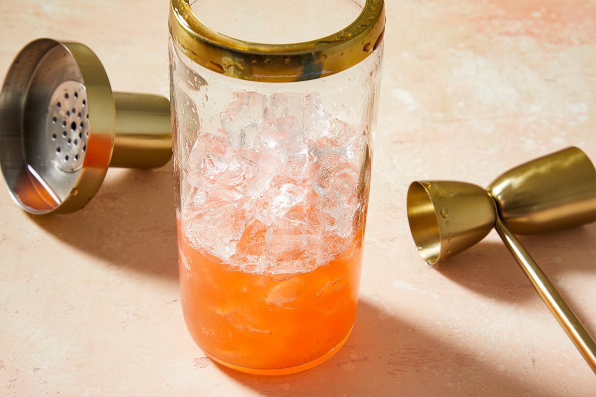 3/4 angle horizontal image of cocktail ingredients being shaken with ice in a shaker for a strawberry lemon drop.
