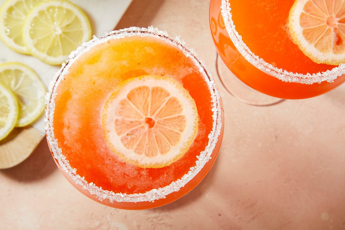 Overhead horizontal image of two strawberry lemon drop cocktails with sugared rims and lemon slices.