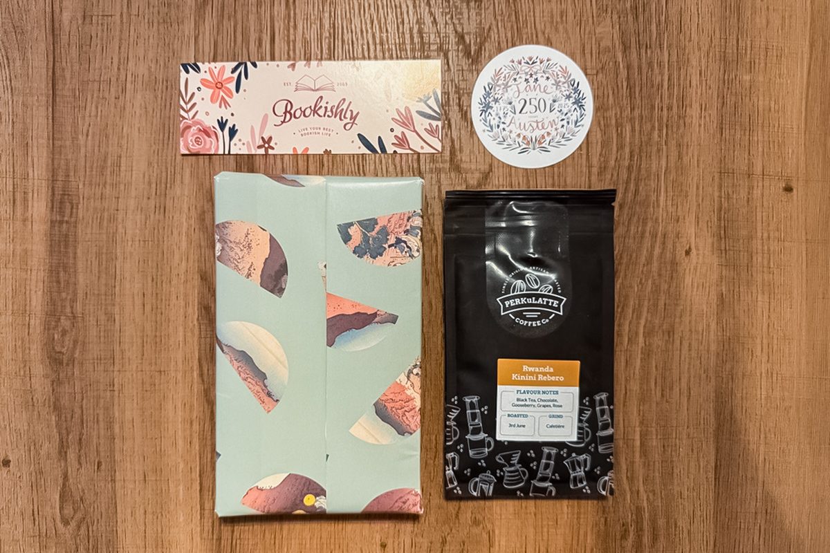A flat lay of a wrapped book with a dessert pattern, a black bag of coffee, a floral 
