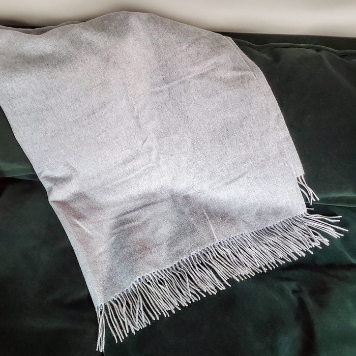 A light gray fringed scarf is spread out on a dark green fabric surface.
