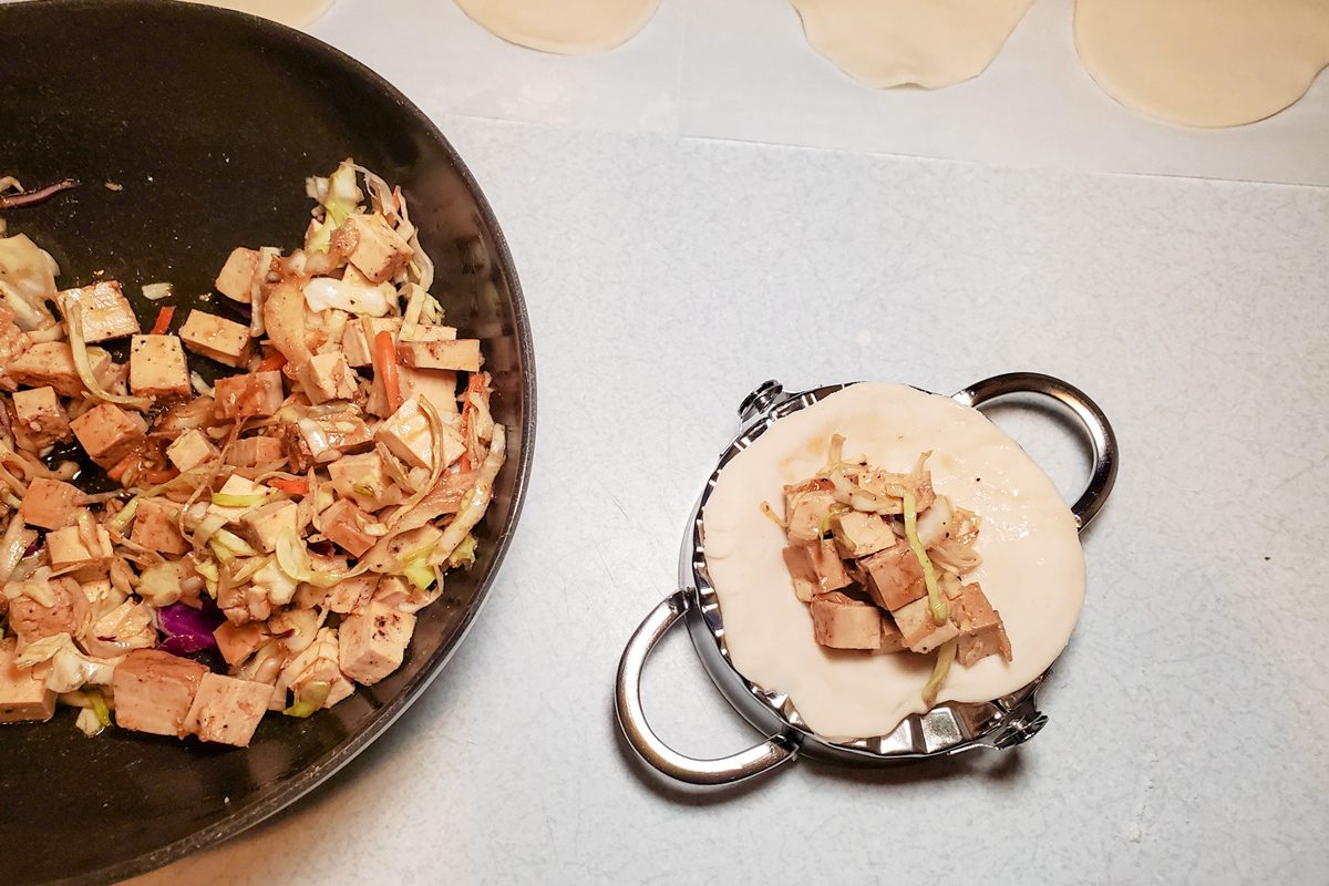 filling placed on a dumpling next to dumpling filling in a large wok