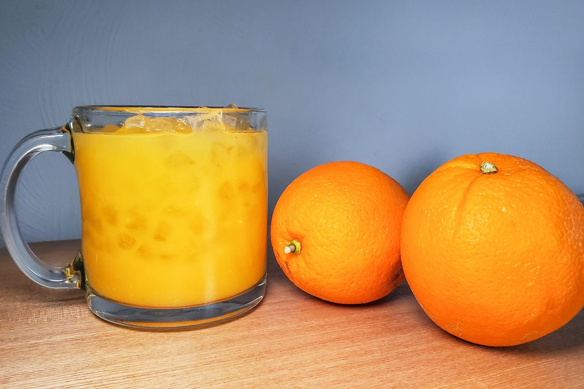 orange juice in glass cup next to two oranges