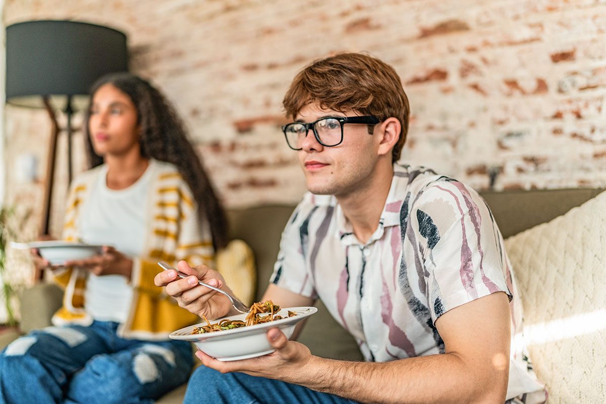 Young man eating and watching tv with friend at home