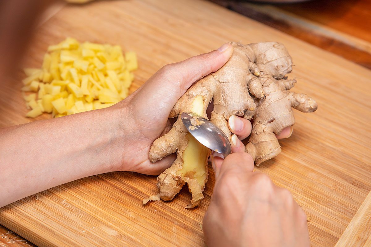 Peeling or peel off ginger with a spoon, preparation in the kitchen, female hands