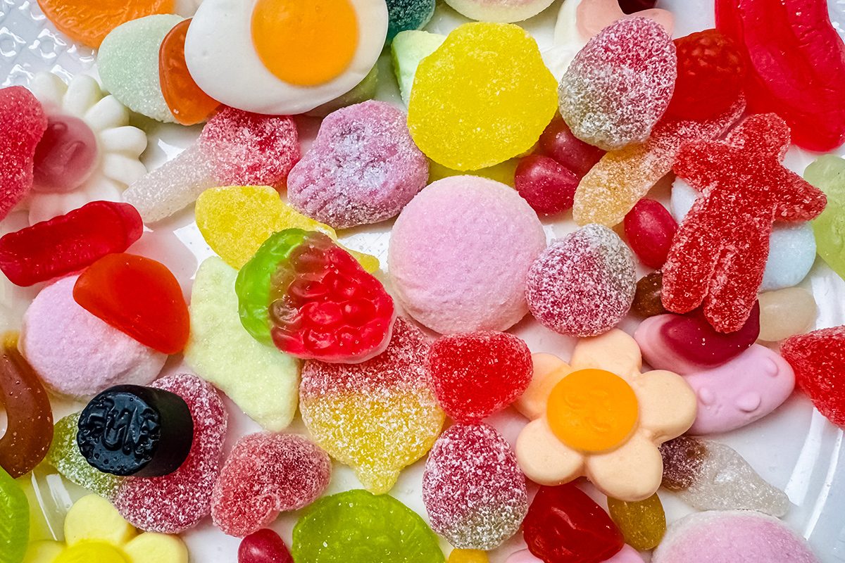 A colorful assortment of gummy candies in various shapes, including flowers, fruits, hearts, and bears, spread out on a white surface.