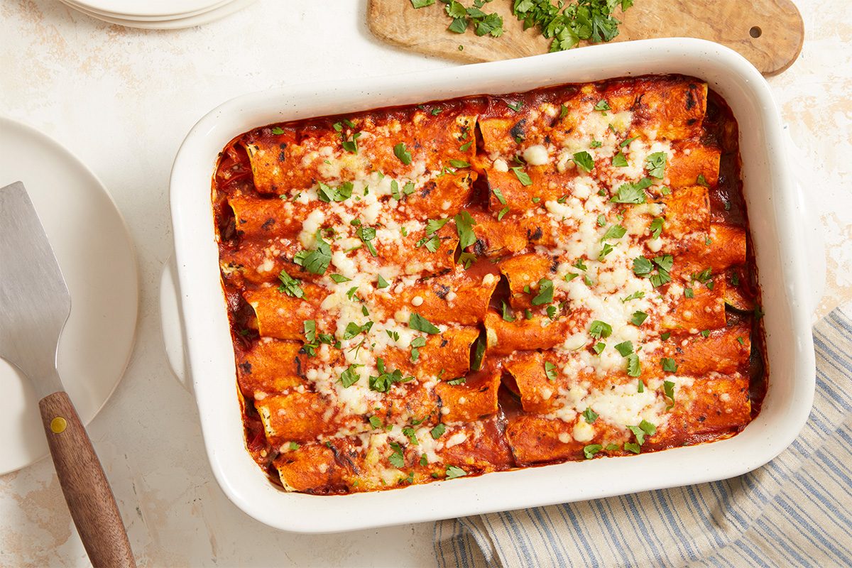 Overhead horizontal image of baked Farmers Market Enchiladas finished with melted cheese and fresh cilantro. This Fast Track beauty shot visual represents the post-bake stage, highlighting texture, color, and garnish. Ideal for print and digital editorial use showcasing completed cooking steps.