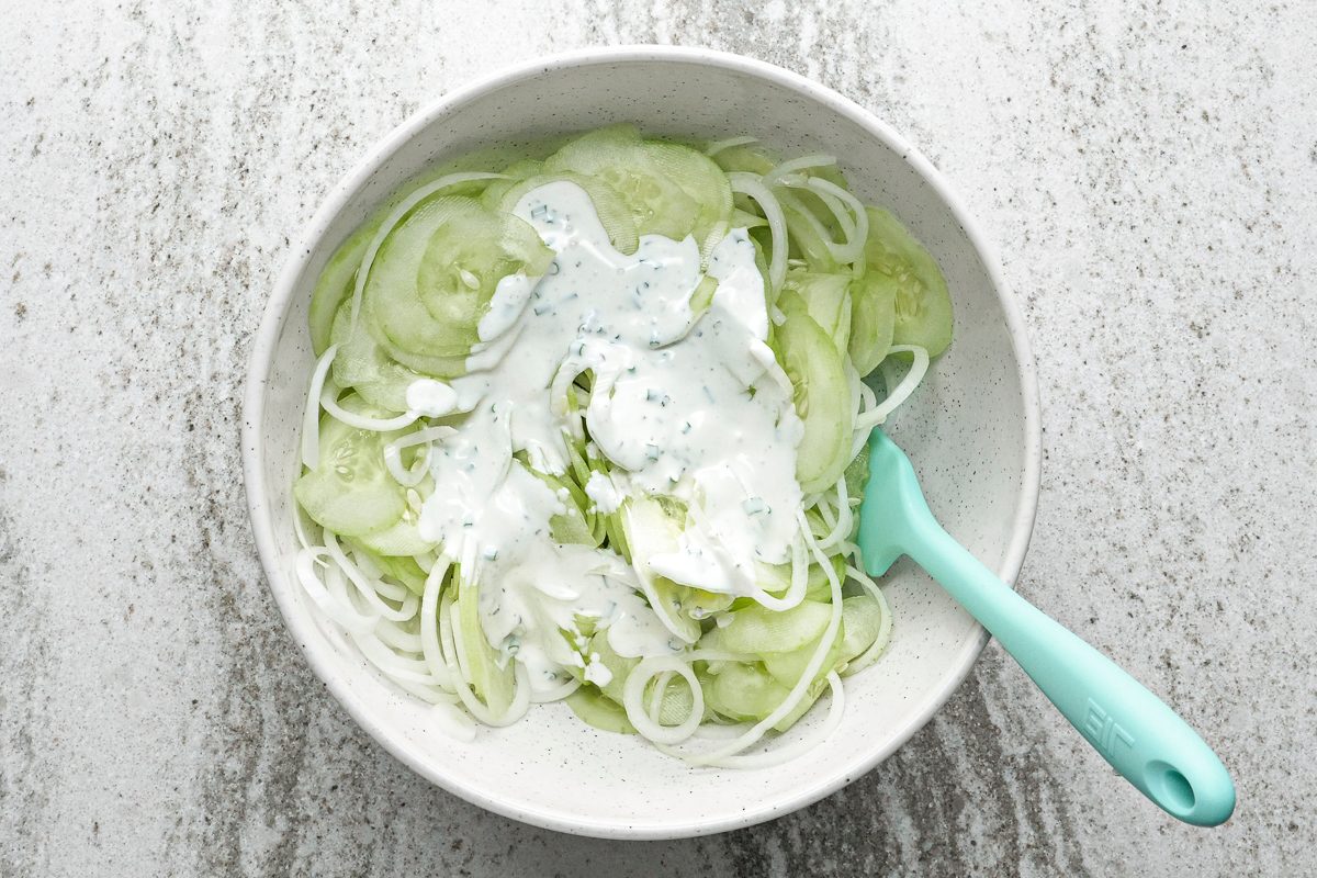 sour cream dressing added to cucumbers and onions in a bowl