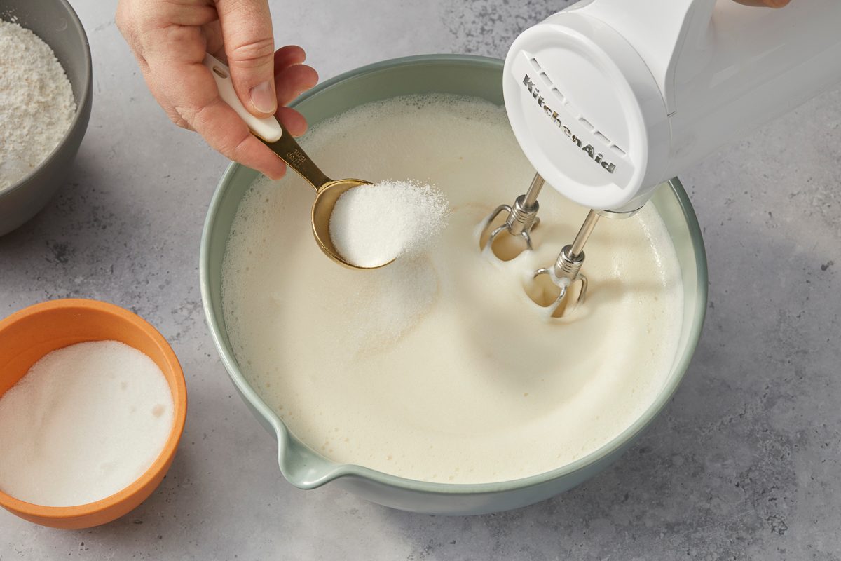 adding granulated sugar to meringue mixture in a large bowl