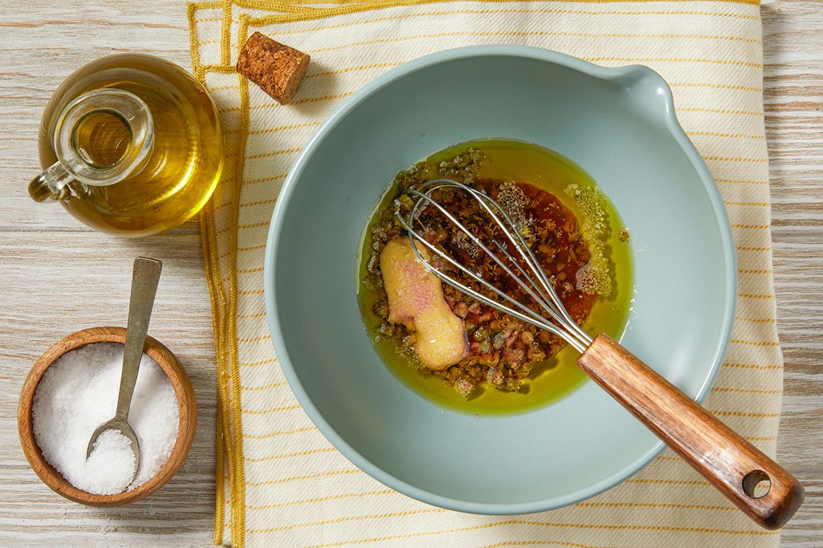 Olive oil, Dijon mustard, red wine vinegar, shallot, and seasonings are whisked together in a bowl to form the vinaigrette.