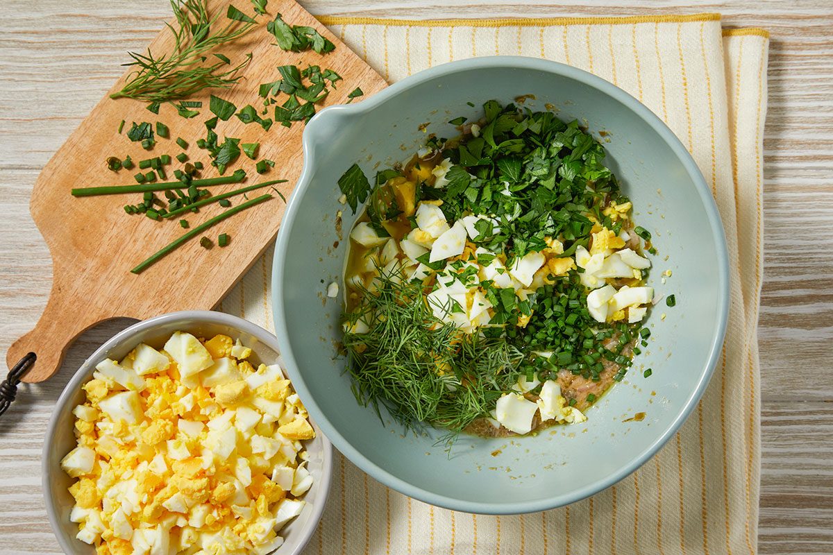 Chopped hard-boiled eggs, parsley, chives, dill, and capers are added to the vinaigrette and mixed.