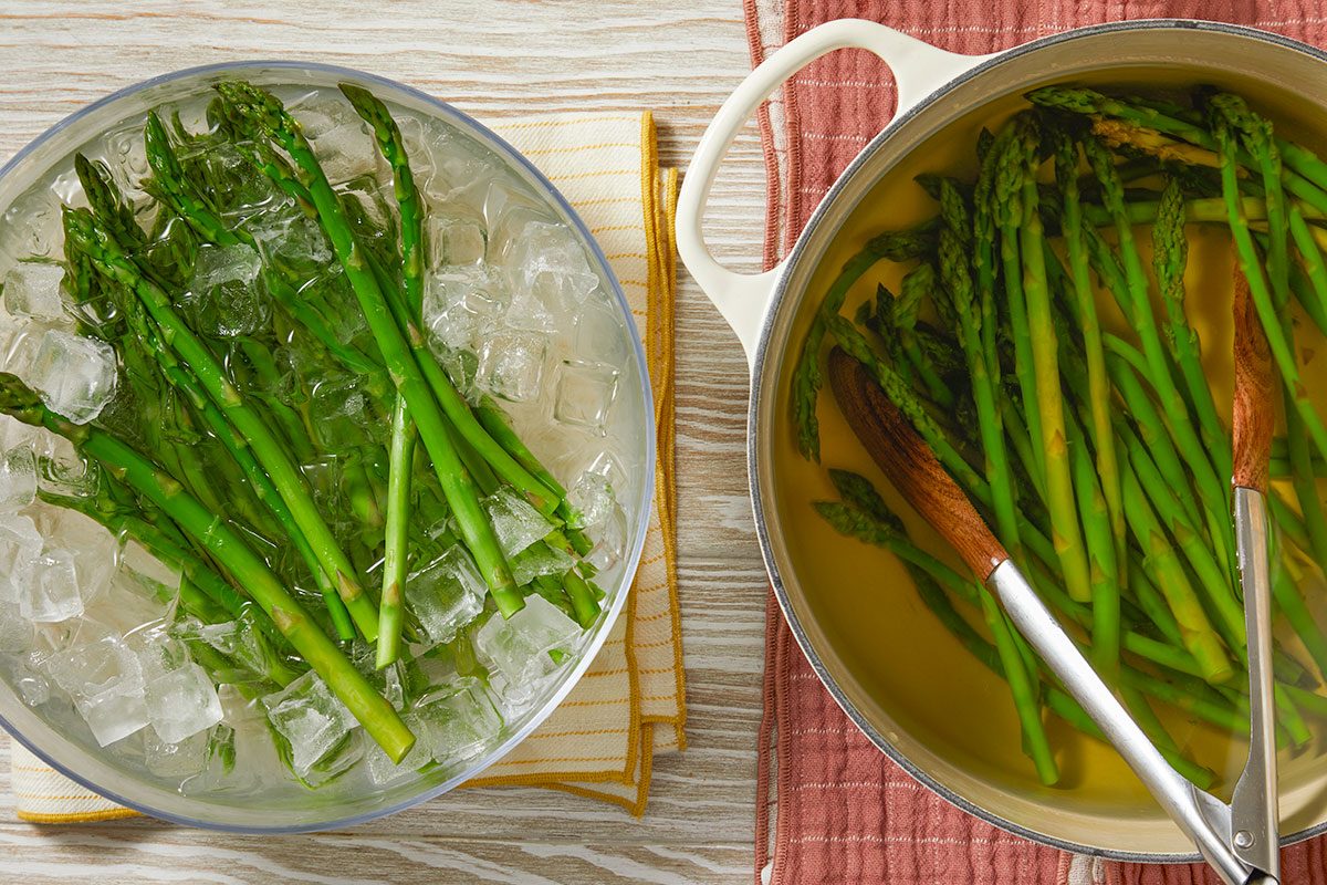Fresh asparagus spears are blanched in boiling water and transferred to an ice bath to stop cooking.