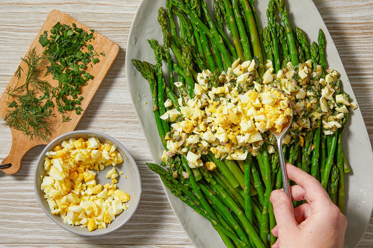 Blanched asparagus is arranged on a platter and topped with the egg and herb vinaigrette mixture.