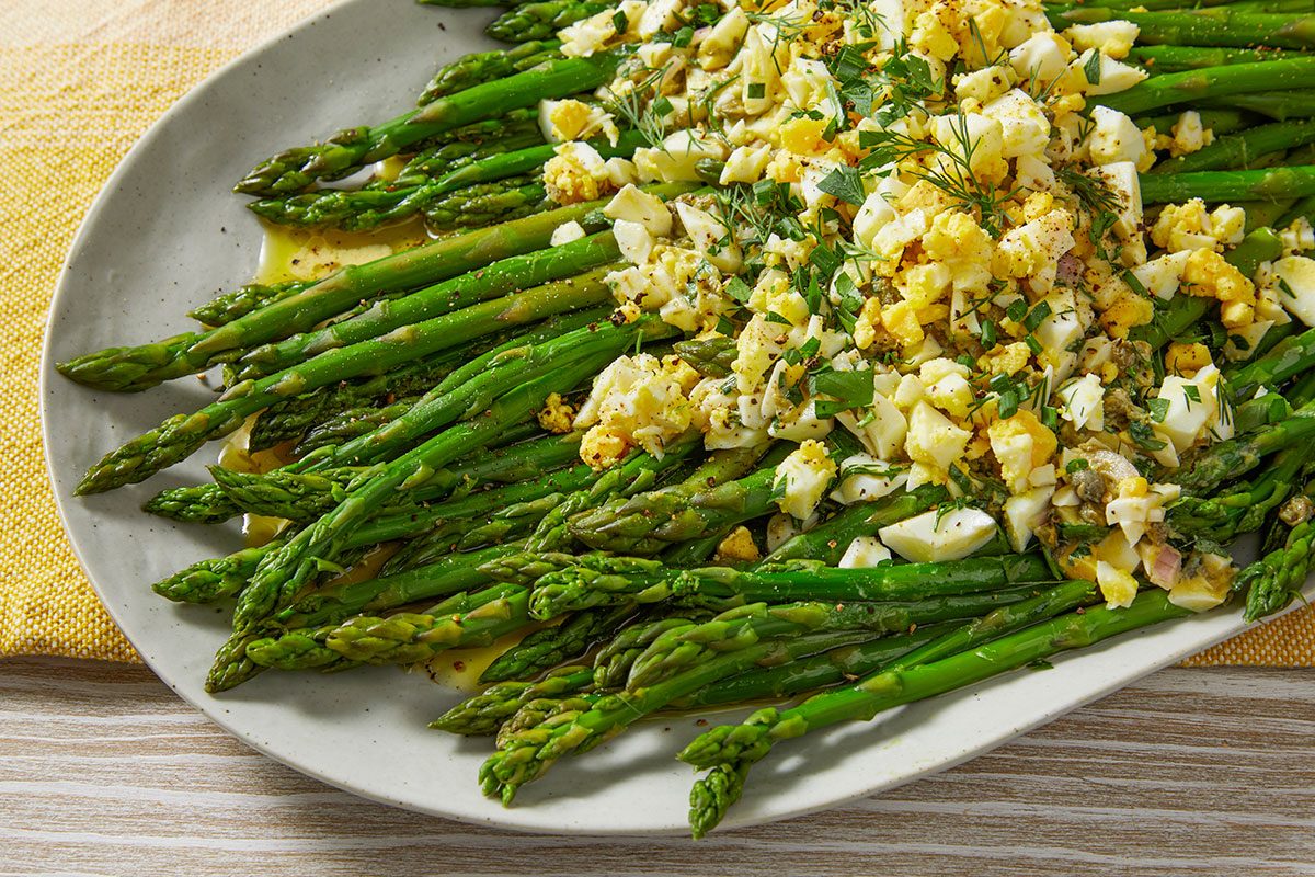 An angled view highlights the texture of asparagus spears topped with egg, herbs, and vinaigrette.