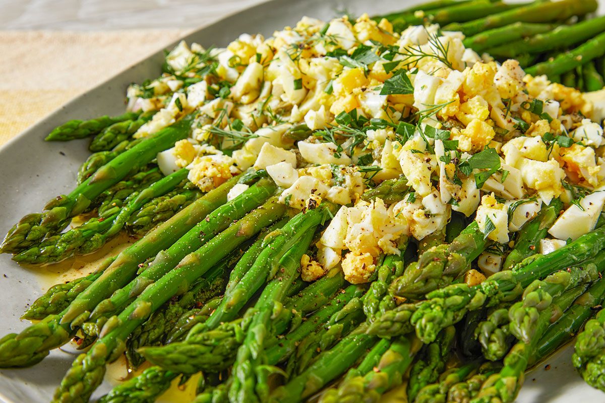 A close-up shows the finely chopped egg, herbs, and vinaigrette coating the asparagus spears.