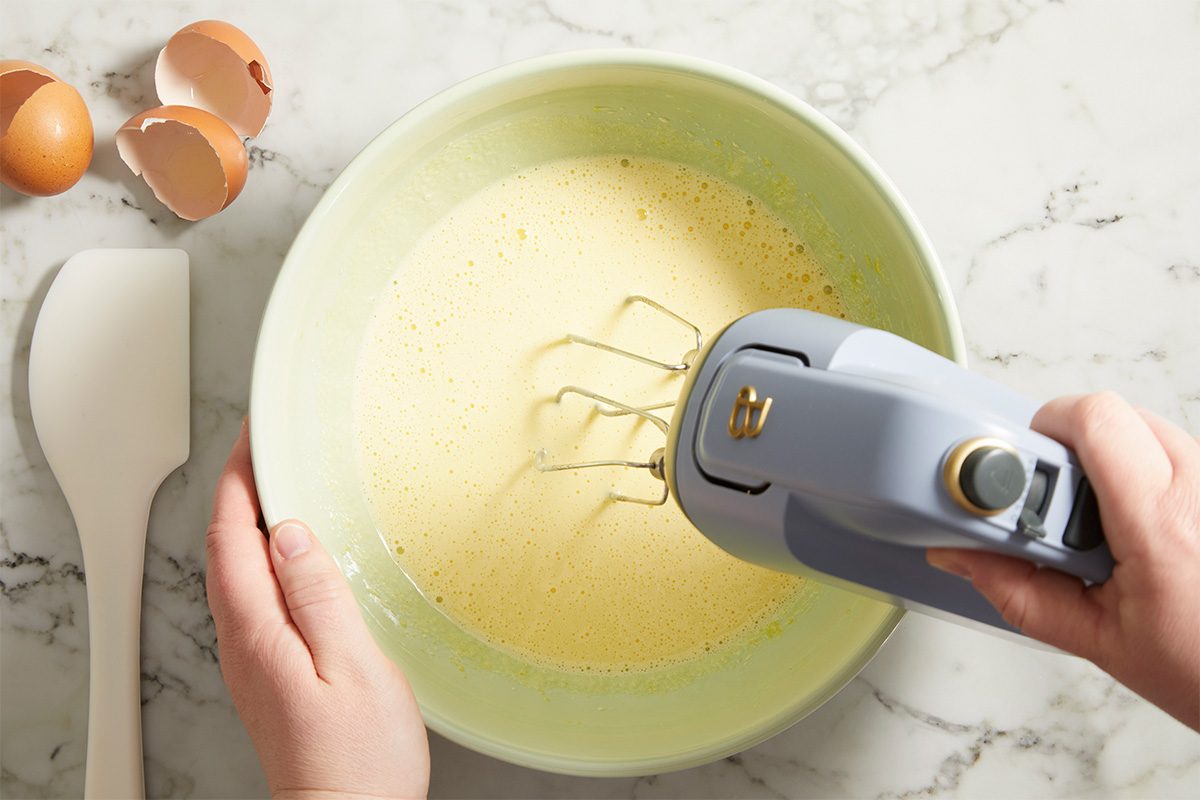 Overhead horizontal image of eggs and sugar being mixed in a bowl with a hand mixer for avocado brownies.