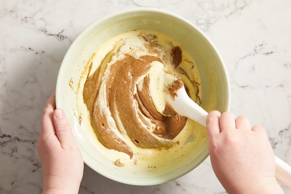 Overhead horizontal image of avocado being incorporated into the brownie batter mixture.