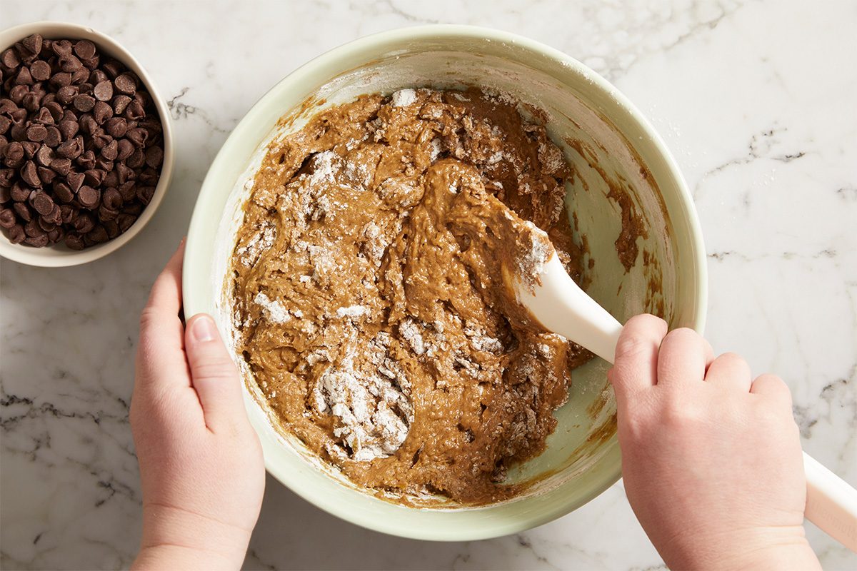 Overhead horizontal image of dry ingredients and chocolate chips being folded into avocado brownie batter.