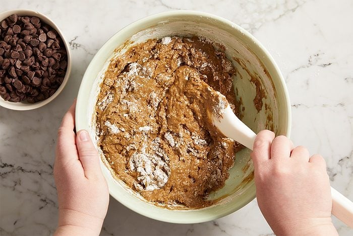 Overhead horizontal image of dry ingredients and chocolate chips being folded into avocado brownie batter.