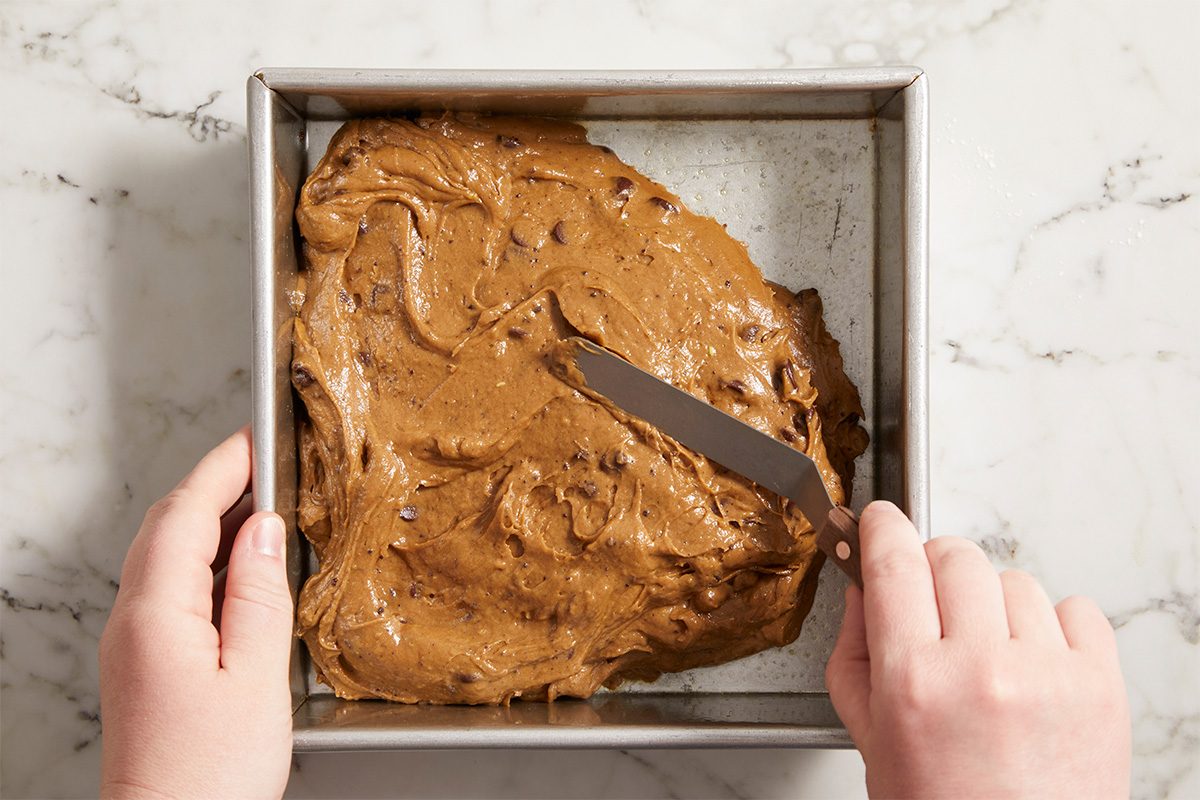 Overhead horizontal image of brownie batter being spread evenly into a baking pan.