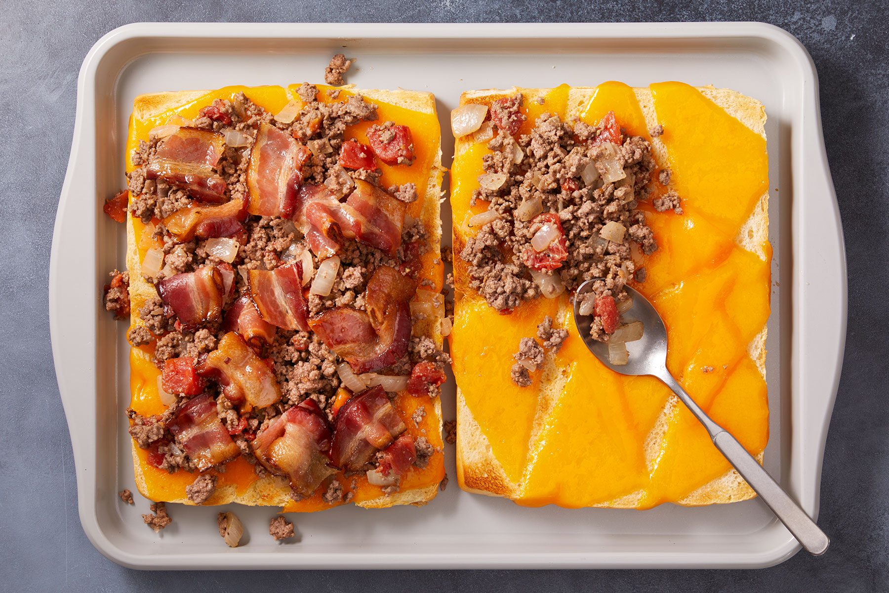 Spooning beef mixture evenly over rolls and topping them with bacon and remaining cheese on a tray.
