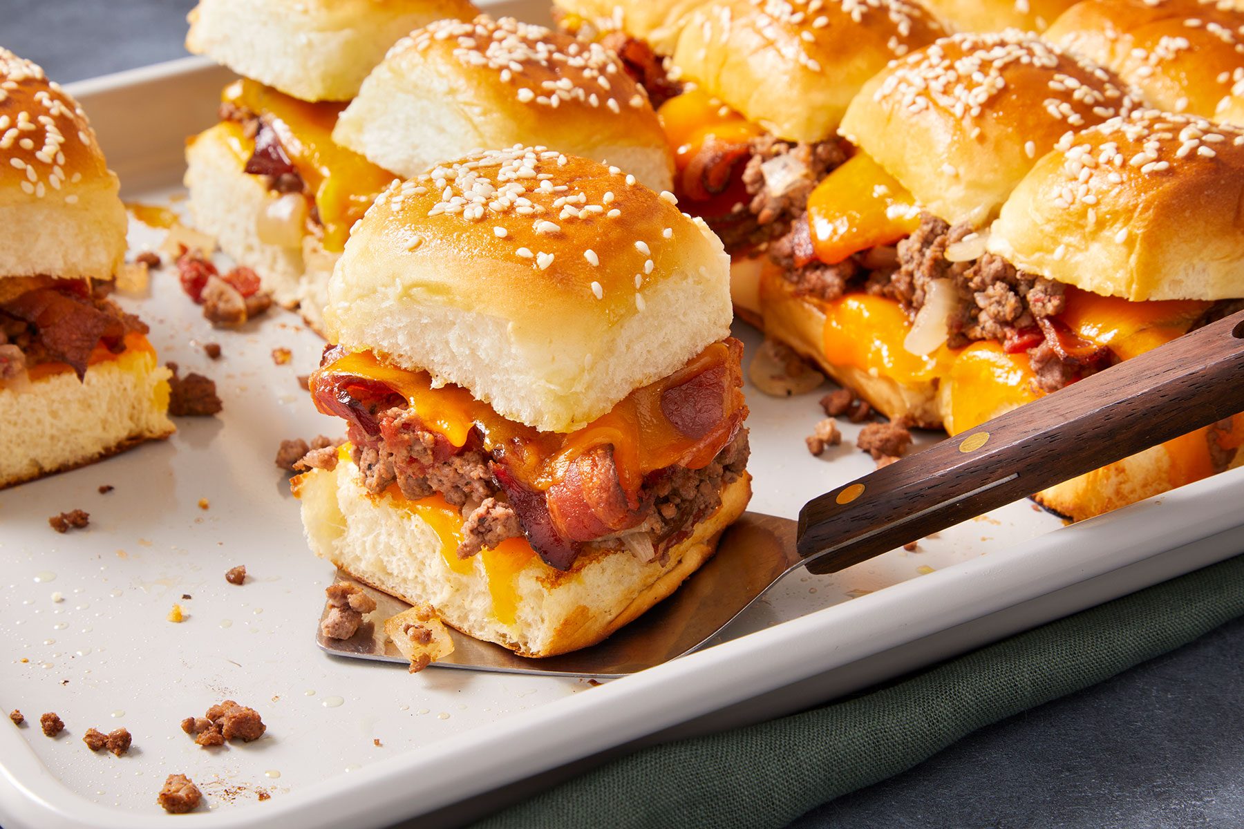Bacon Cheeseburger Sliders on a tray with one being lifted with a serving knife.