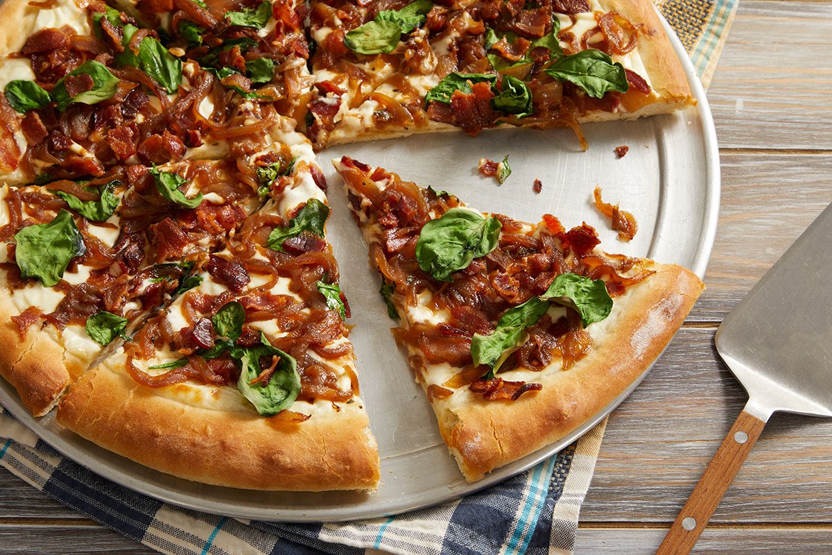 Overhead shot of a sliced bacon and spinach pizza on a pizza pan