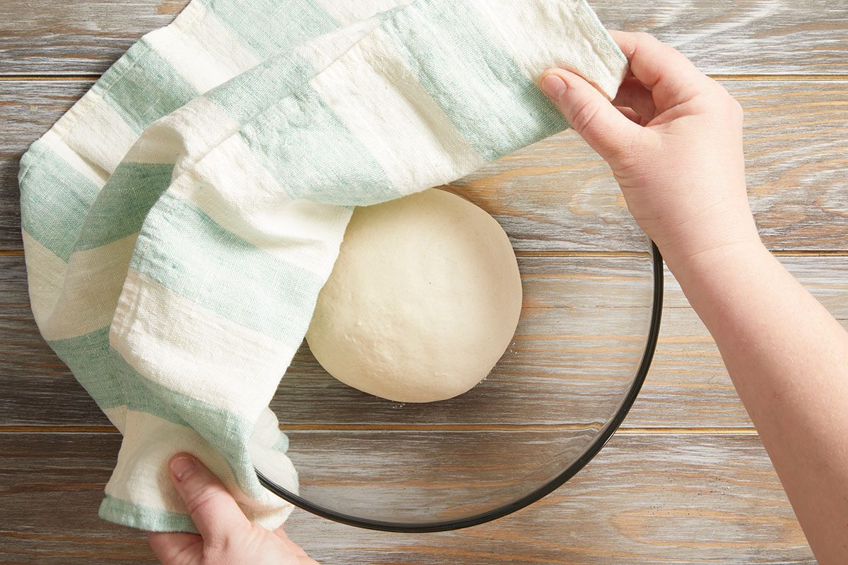 Overhead shot of a person covering a ball of dough in a bowl