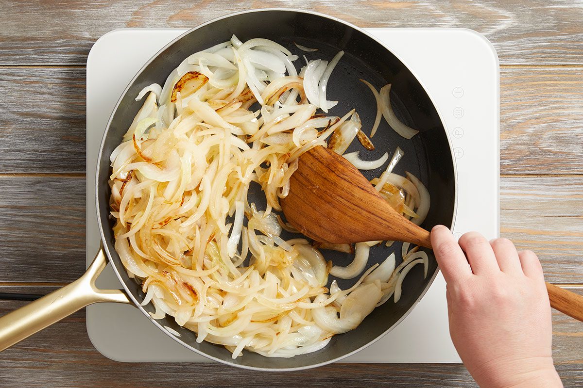 Overhead shot of a hand stirring sliced onions in a frying pan