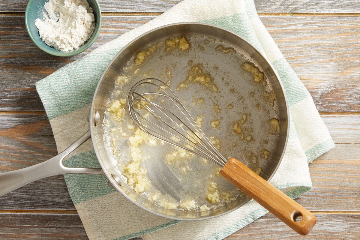 Overhead shot of a whisk in a saucepan with melted butter and flour 