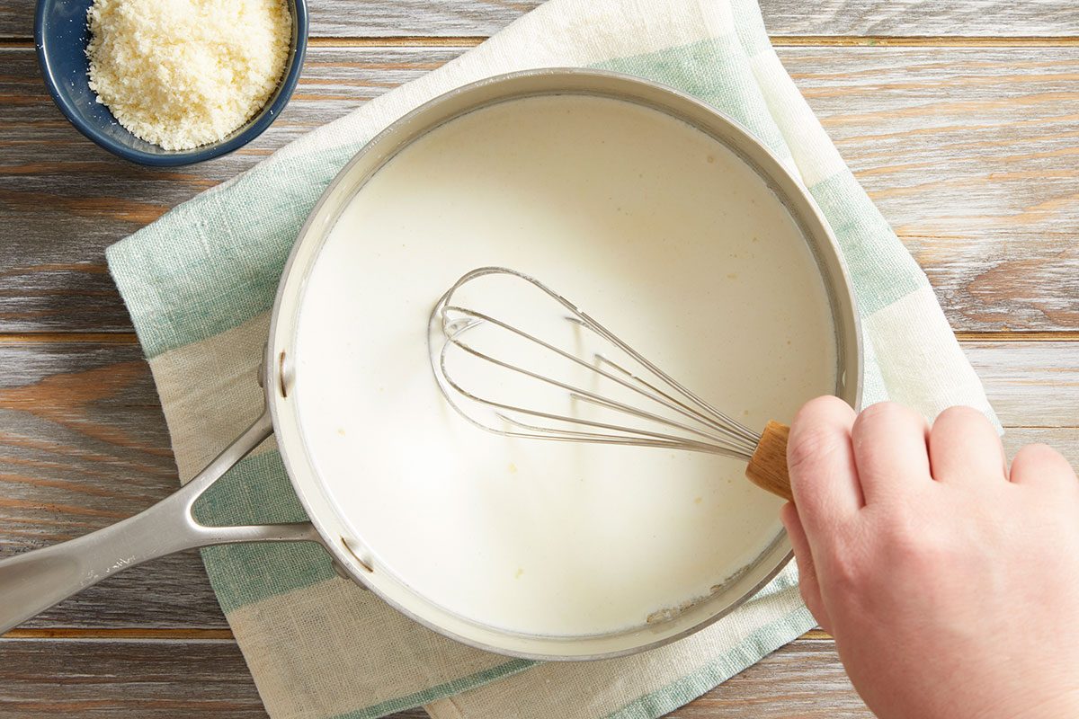 Overhead shot of a hand whisking a creamy white sauce