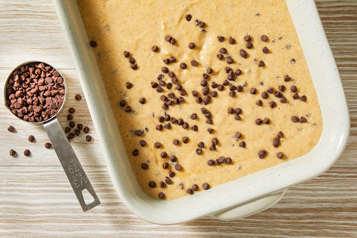 A horizontal overhead image shows banana chocolate chip batter spread in a rectangular baking dish with chocolate chips sprinkled across the top.