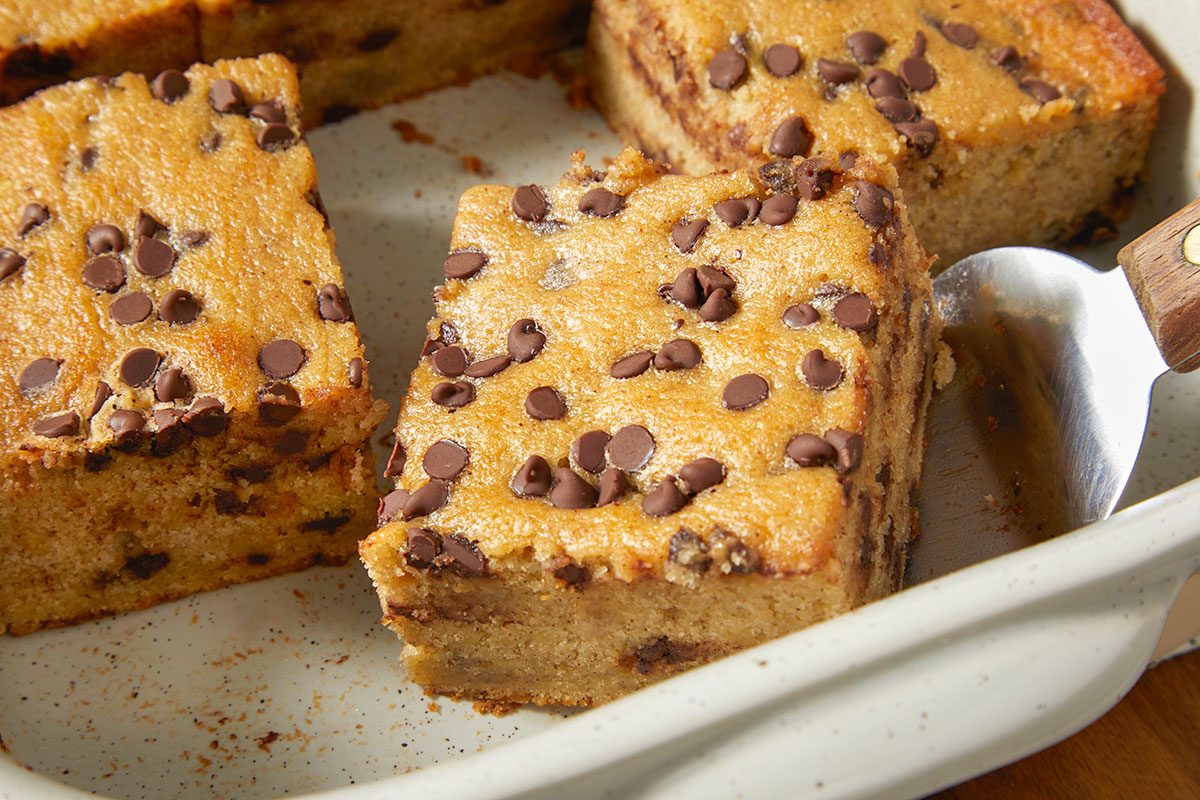 A horizontal close-up image shows thick squares of banana chocolate chip cake with visible chocolate chips and moist crumb texture inside a baking dish.