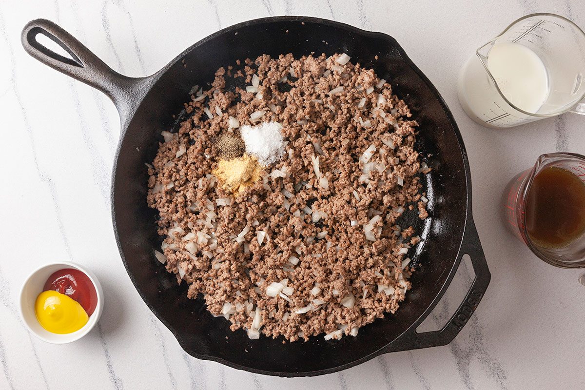 Ground beef is cooked with onion and seasonings in a skillet, with broth and milk added to create a savory base.