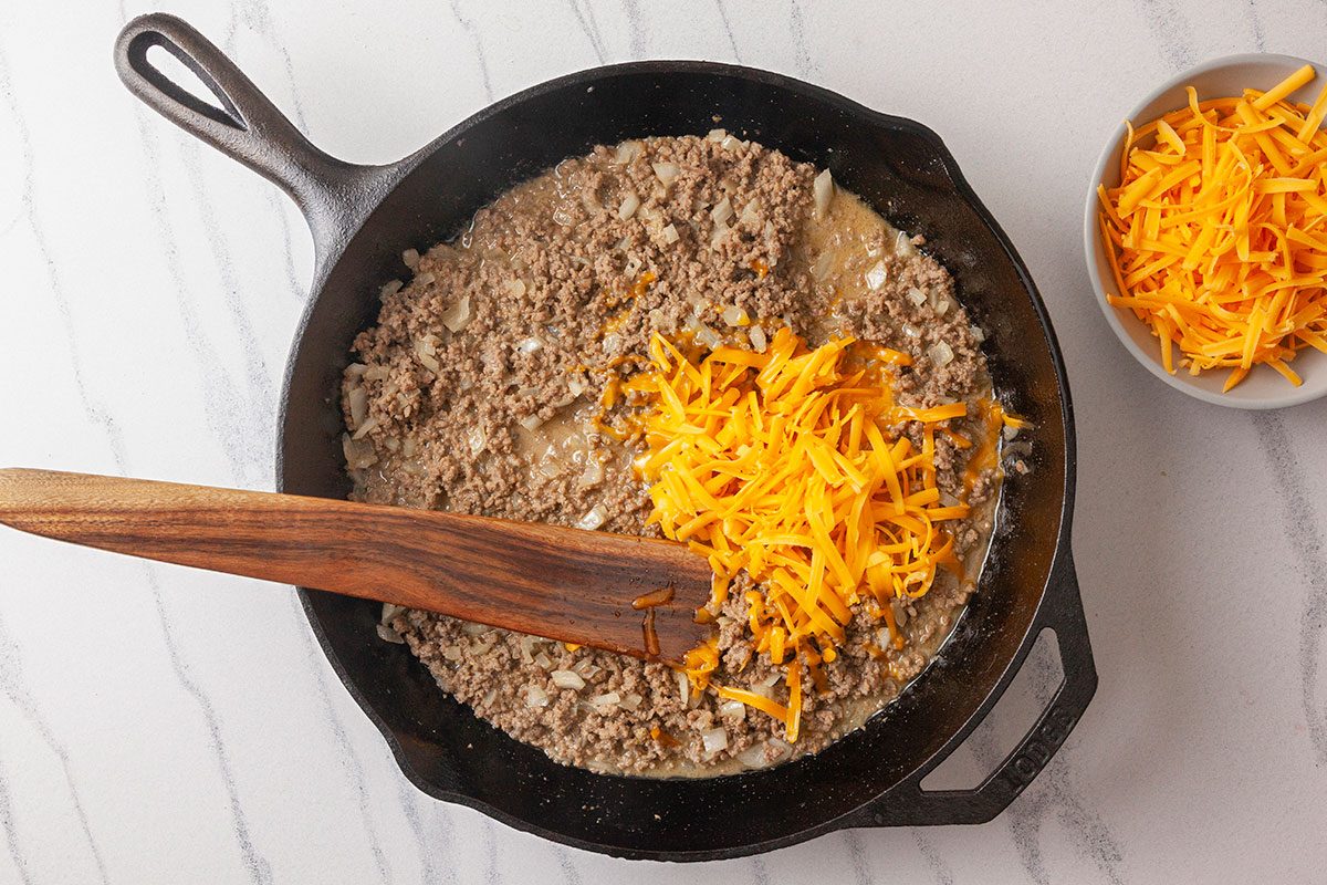 Shredded cheddar cheese is added to the cooked beef mixture and stirred to melt.