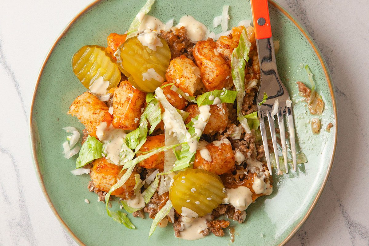 A close-up of the plated casserole highlights crispy tater tots, seasoned beef, and fresh toppings.