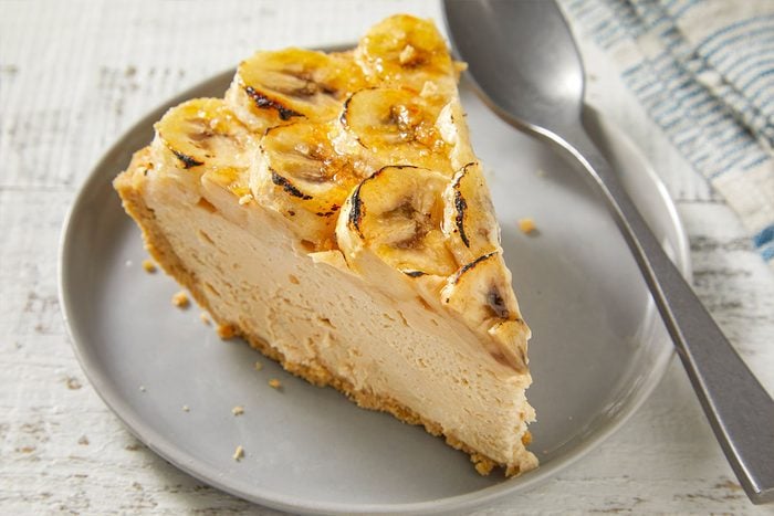 Eye Level horizontal image of a slice of banana cream pie on a gray plate with a spoon. The pie is topped with caramelized banana slices.