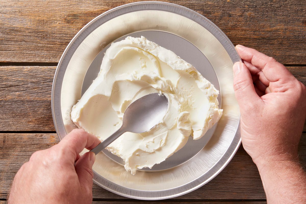 Spreading softened cream cheese in the bottom of a 9-inch disposable foil pie pan