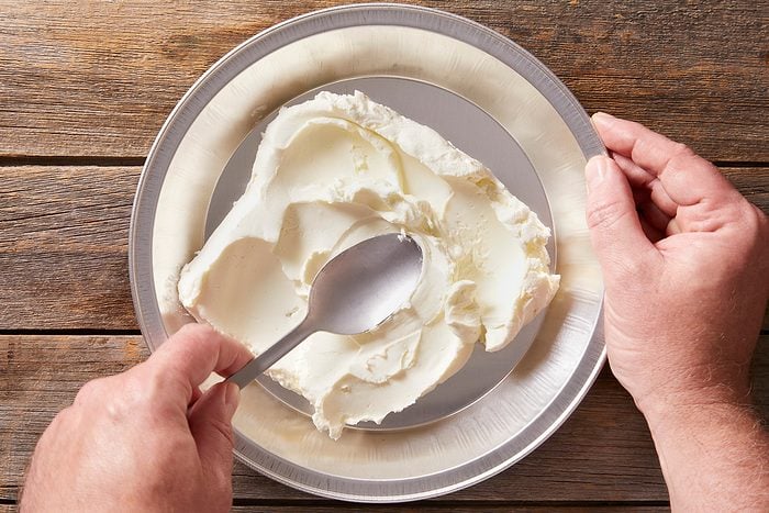 Spreading softened cream cheese in the bottom of a 9-inch disposable foil pie pan