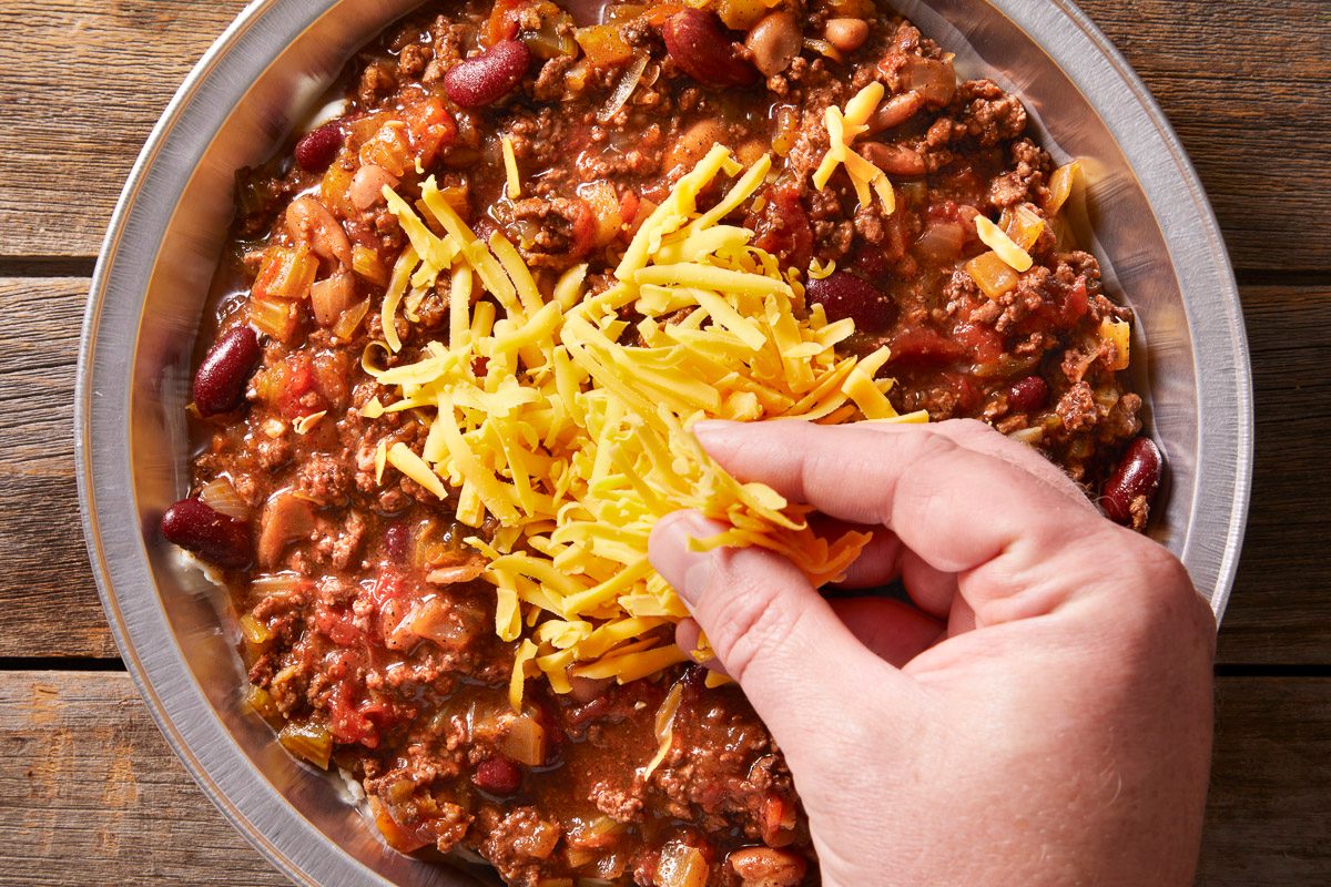 adding shredded cheese to chili with beans