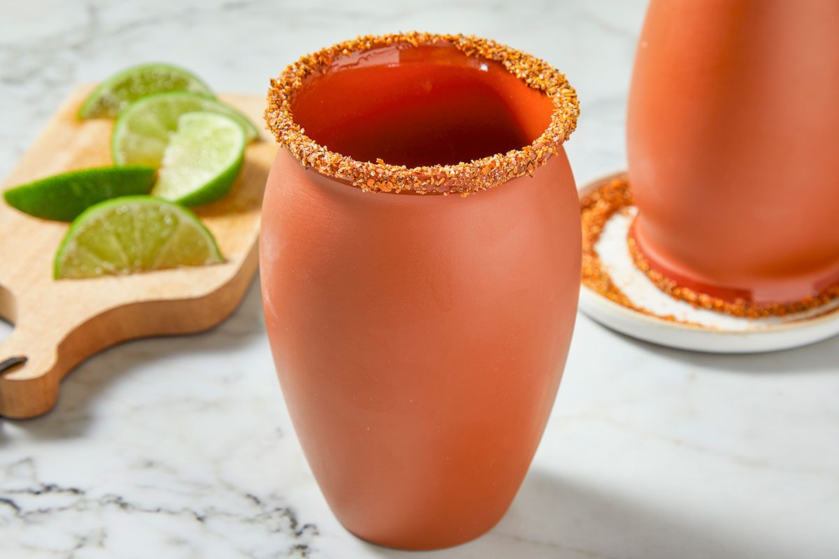 Clay cantarito glasses are prepared with a Tajín- and salt-rimmed edge, styled with fresh lime wedges on the side.